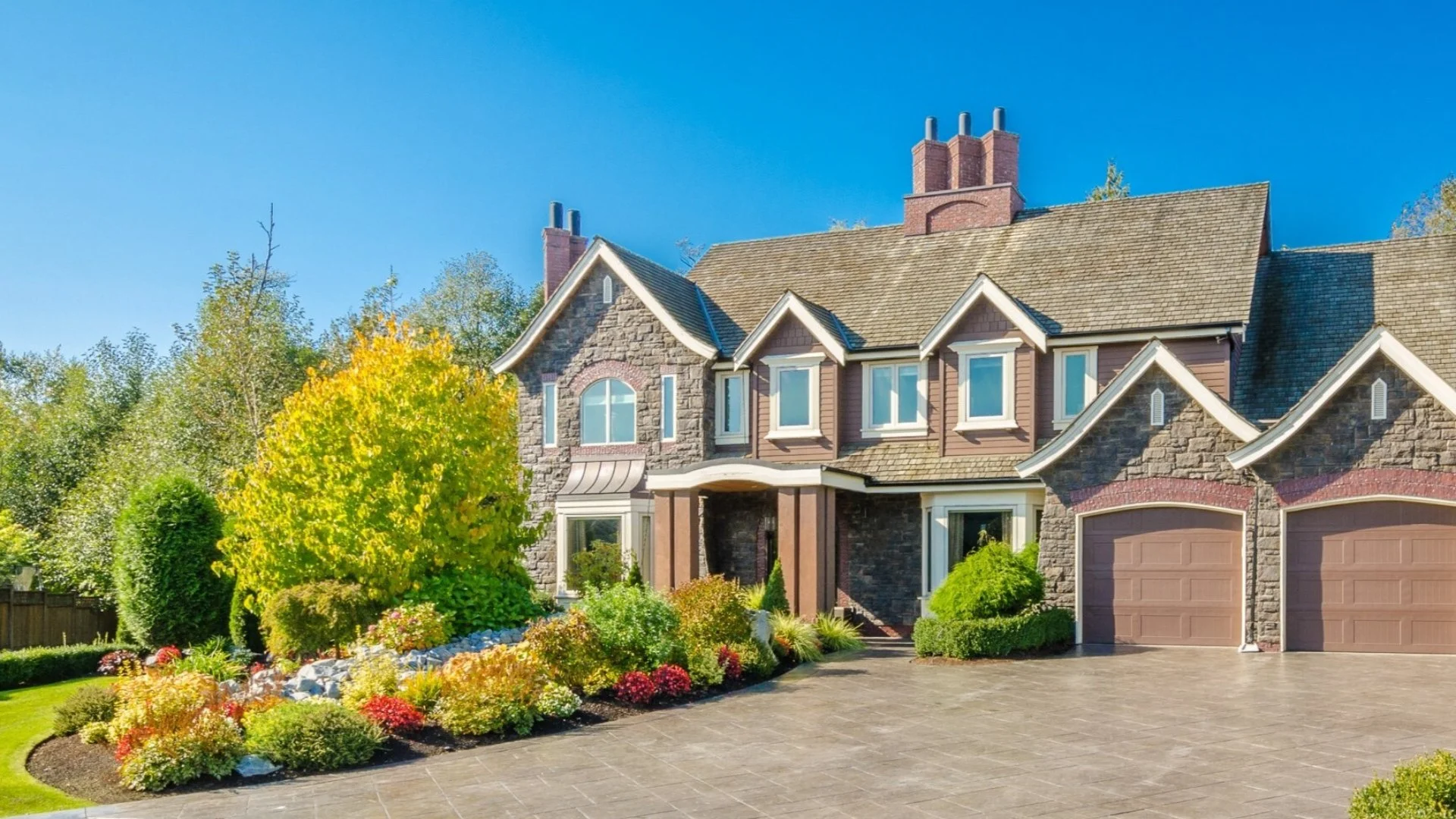 A beautiful luxury estate home with stone and wood exterior, a spacious driveway, and vibrant landscaping in Huron, OH.