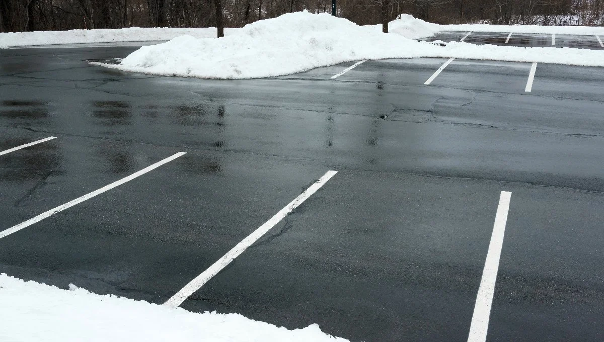 A mostly empty parking lot covered in snow with wet pavement reflecting the surroundings. Huron, OH.